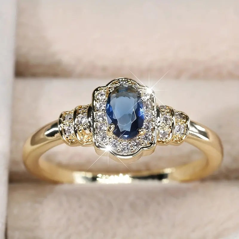 Elegant 18K gold-plated promise ring with a central blue gemstone surrounded by sparkling cubic zirconia.